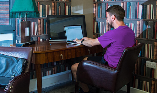 A man is sat working at a laptop in a home office.