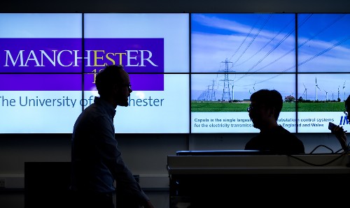 Research staff in front of digital screen showing University of Manchester logo